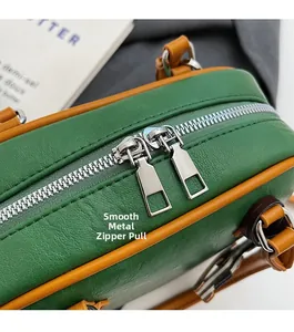 Detail of smooth silver dual metal zippers on green pebble leather crossbody handbag