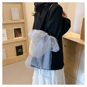 Straw woven handbag with light blue mesh bow shown on shoulder in a lifestyle setting