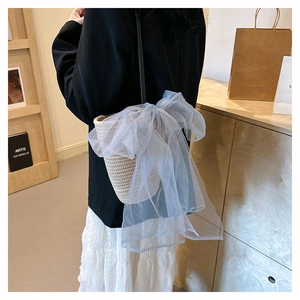 Detail of hand-woven straw bucket bag featuring a large light blue mesh bow decoration