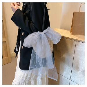 Detail of woven straw bucket bag featuring a large mesh bow and black leather strap