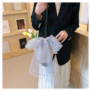 Close-up of woven straw bucket bag featuring a large grey mesh bow and leather strap