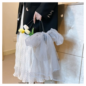 Close-up of woven straw handbag featuring a large grey mesh bow and black leather handle