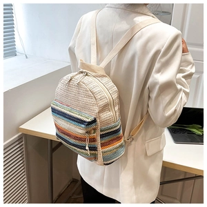 Detail of woven beige backpack with colorful stripes shown on model wearing white blazer