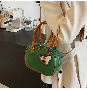 Deep green Boston bag with orange trim and rocking horse charm in a cafe setting