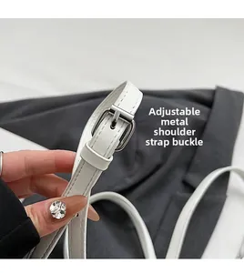Detail view of the adjustable polished silver buckle and white leather strap on a handbag