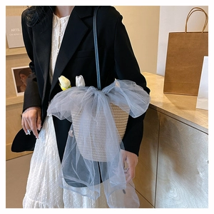 Detail of woven straw bucket bag with a large grey mesh bow and black leather strap