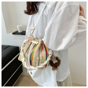 Detail of rainbow striped woven bucket bag with leather strap and plush monster charm