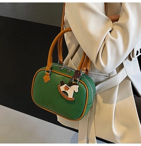 Close-up of retro green PU leather bag with orange trim and cute rocking horse charm