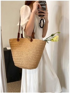 Detail of straw woven tote bag with dark brown leather straps on a model in white dress