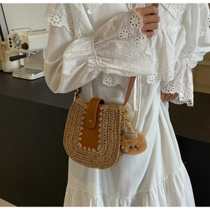 Close-up of woven straw crossbody bag featuring brown leather trim and cute plush charm