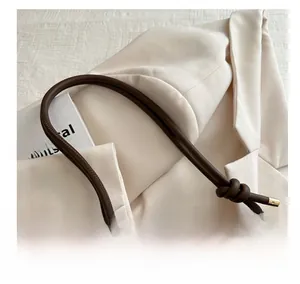 Detailed view of brown crossbody bag featuring colorful wave embroidery and knotted strap