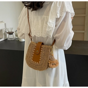Detail view of woven straw crossbody bag with brown leather flap and cute plush charm