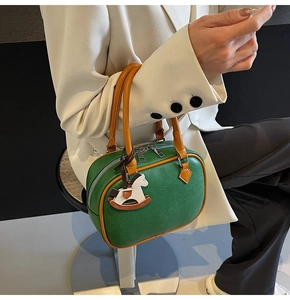Detail of green PU leather handbag with orange trim and decorative rocking horse charm