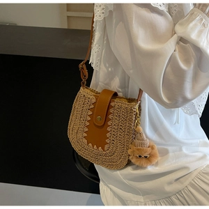 Detail of straw woven crossbody bag featuring a brown leather strap and cute bear charm