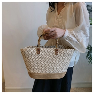 Detail of woven straw tote bag featuring natural bamboo handles and textured bicolor pattern