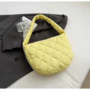 Pale yellow quilted nylon shoulder bag with wavy stitching on grey suit background