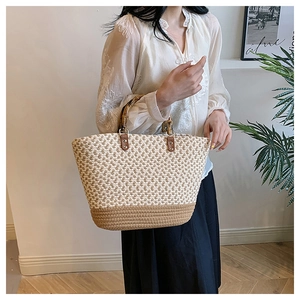Detail of woven straw tote bag with natural bamboo handles and contrast stitching