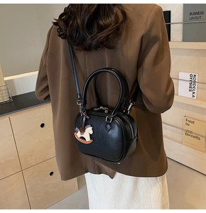 Detail of black semi-round PU leather Boston bag with a horse charm on a shoulder strap