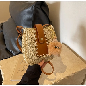 Handwoven straw crossbody bag with brown leather flap and cute monster plush keychain