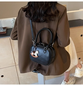 Close-up of black PU leather crossbody bag with wooden horse charm and top handles