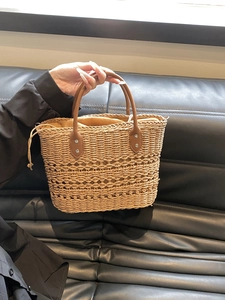 Close-up of woven straw handbag texture featuring brown leather handle and drawstring liner