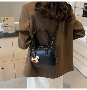 Detail of minimalist black PU leather crossbody bag featuring a wooden rocking horse charm