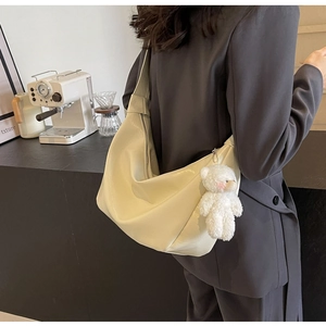 Dettaglio borsa a mezzaluna bianco crema con ciondolo a forma di orsetto sulla tracolla