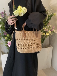 Close-up of woven straw handbag with brown leather handles and metallic rivet details