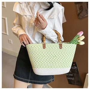 Detail of woven handbag featuring green white patterns and natural bamboo handles