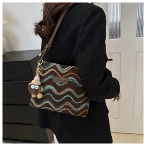 Detail of a brown knit crossbody bag featuring wavy patterns and a cute monster charm