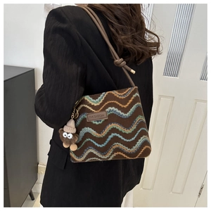 Detail of brown woven crossbody bag with colorful waves and a cute plush monster charm
