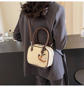 Detail view of cream white Boston bag with brown handles and a small wooden horse charm