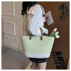 Detail of woven tote bag with bamboo handles and green-beige color block pattern