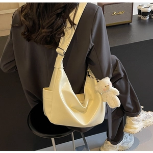 Dettaglio della borsa a mezzaluna bianco crema in ecopelle morbida con ciondolo a orsetto