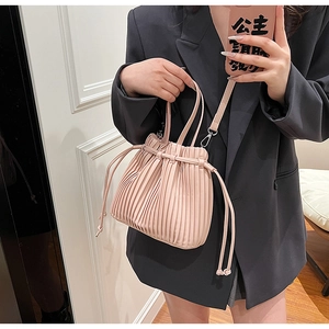 Pink pleated bucket bag with drawstring closure and crossbody strap in lifestyle view