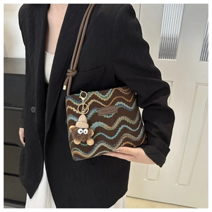 Close-up of brown textured knit crossbody bag featuring a cute plush monster charm