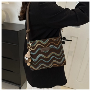 Close-up of wavy woven crossbody bag with brown leather FASHION label and plush monster charm