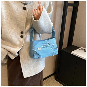 Détail du sac à bandoulière en denim bleu clair avec badges métalliques en cœur et étoile