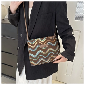 Detail of dark brown plush crossbody bag featuring colorful wave embroidery and leather tag