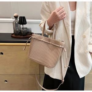 Detail of beige pleated bucket bag showing vertical textures and adjustable shoulder strap