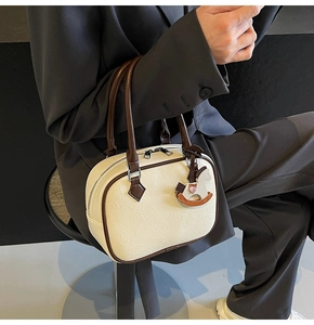 Detail of cream PU leather handbag featuring brown handles and wooden pony charm accent