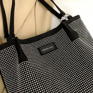 Detailed close-up of a black suede tote bag with shiny silver rhinestones and fashion label