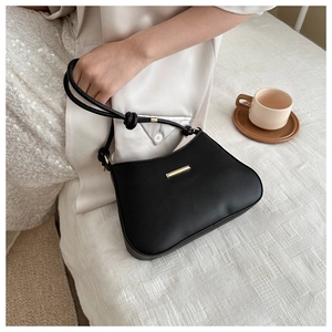 Detail of black underarm bag with gold metal trim and knotted strap design