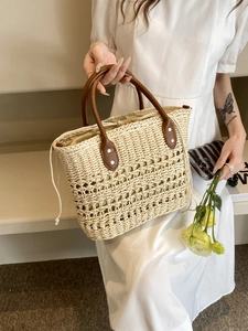 Detail of hand-woven straw tote with brown leather handles and secure silver rivets