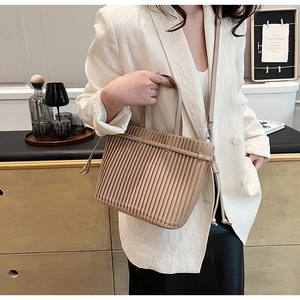 Detail of beige pleated faux leather bucket bag worn by model in elegant white blazer