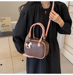 Detail of a brown PU leather Boston bag with pink handles and a white rocking horse charm