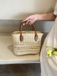 Detailed view of woven straw tote bag featuring brown leather handles and silver metal rivets