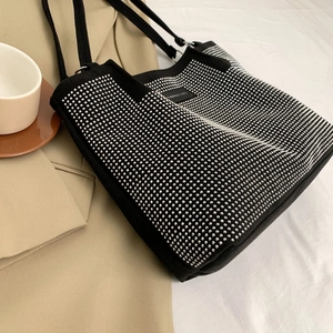 Detail of black tote bag featuring silver rhinestone studs and woven handles