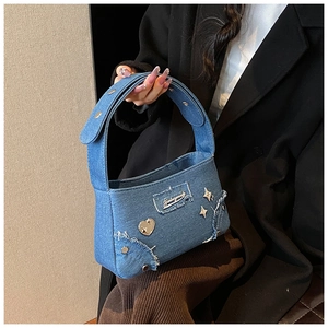 Détail du sac bandoulière en denim bleu avec rivets cœur et bordures effilochées