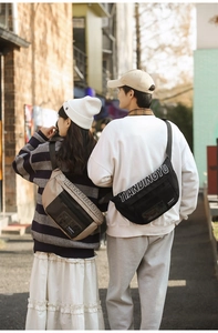 Sac banane tendance en mesh de nylon beige et noir porté par des modèles en extérieur